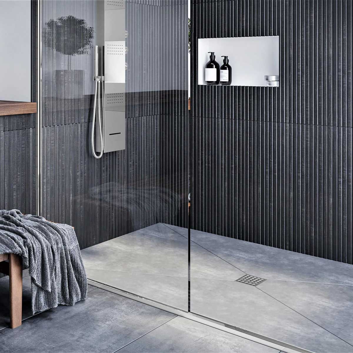 Modern shower with glass door, tiled walls, and a bench with a towel and Ebbe Square Shower Drain Grates Matte Black PVD