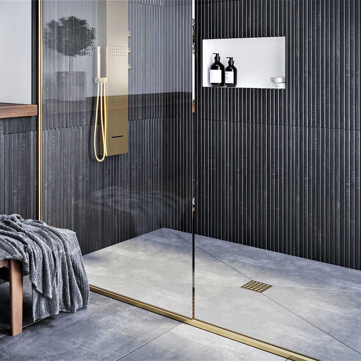 Modern shower with glass door, tiled walls, and a bench with a towel and Ebbe Square Shower Drain Grates