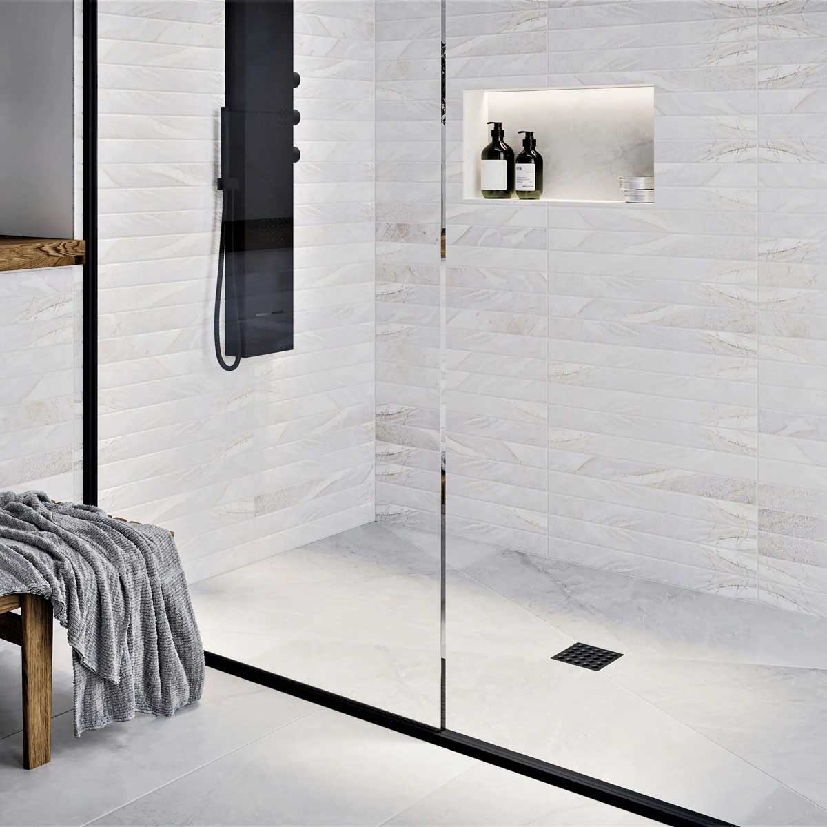Modern shower with glass door, tiled walls, and a bench with a towel and Ebbe Square Shower Drain Grates Matte Black PVD