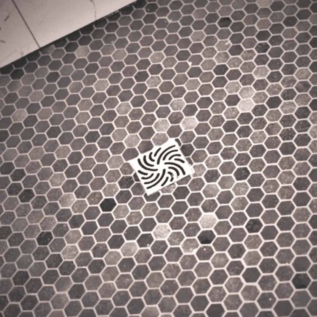 Hexagonal tile floor with a Ebbe Drains Unique Square Shower Drain Grate - Twister In brushed Nickel