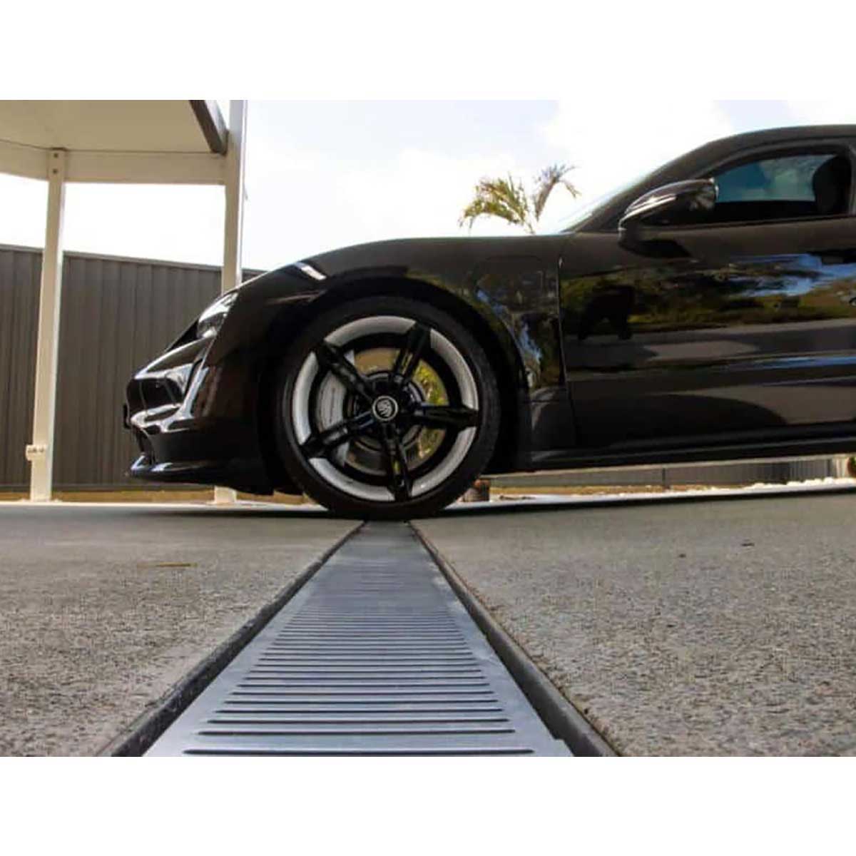 Black sports car approaching a Lauxes Grates Custom Linear Shower Drain NeXT Generation Midnight Black