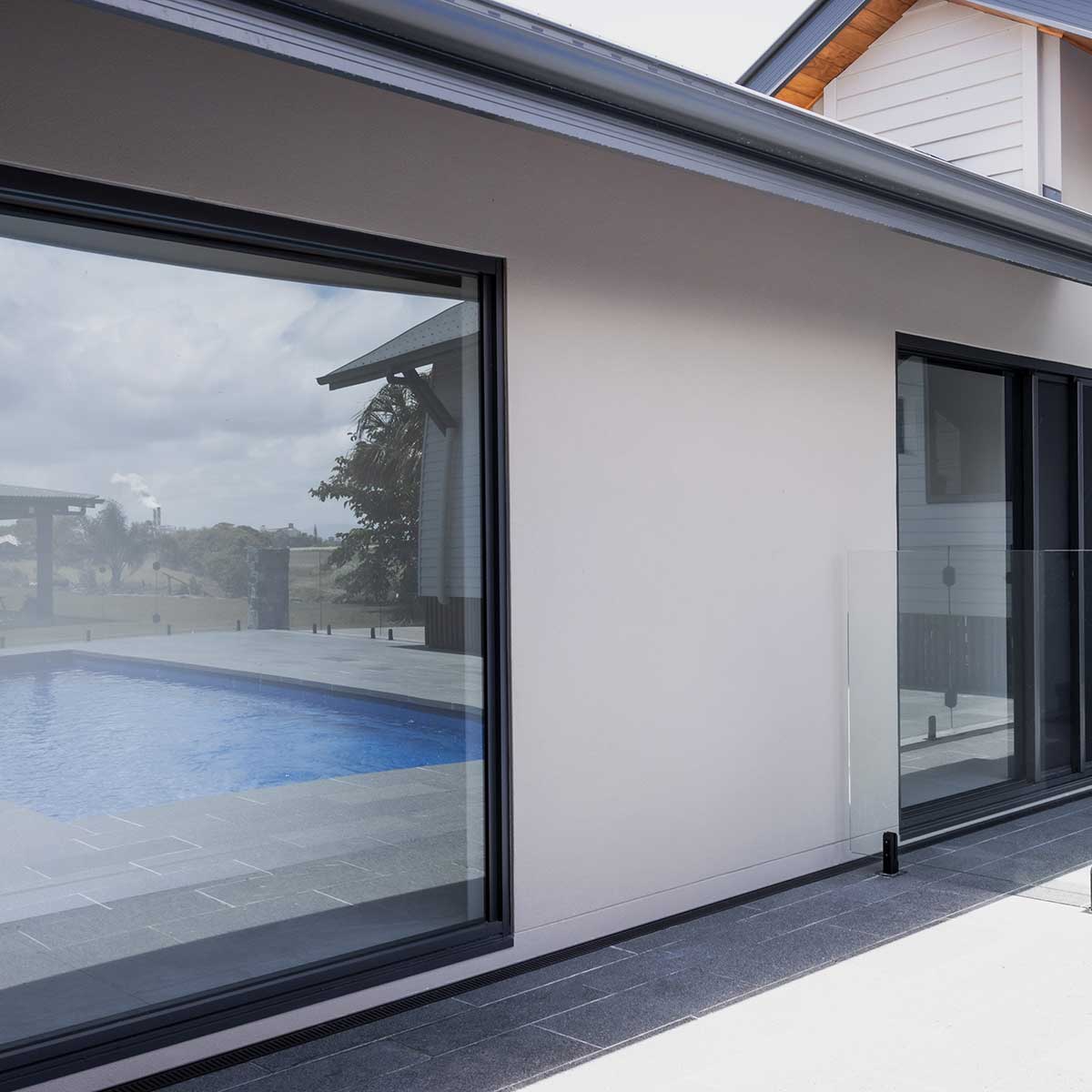 Modern house exterior with large glass windows overlooking a pool with Lauxes Grates Custom Linear Shower Drain NeXT Generation Midnight Black Installed