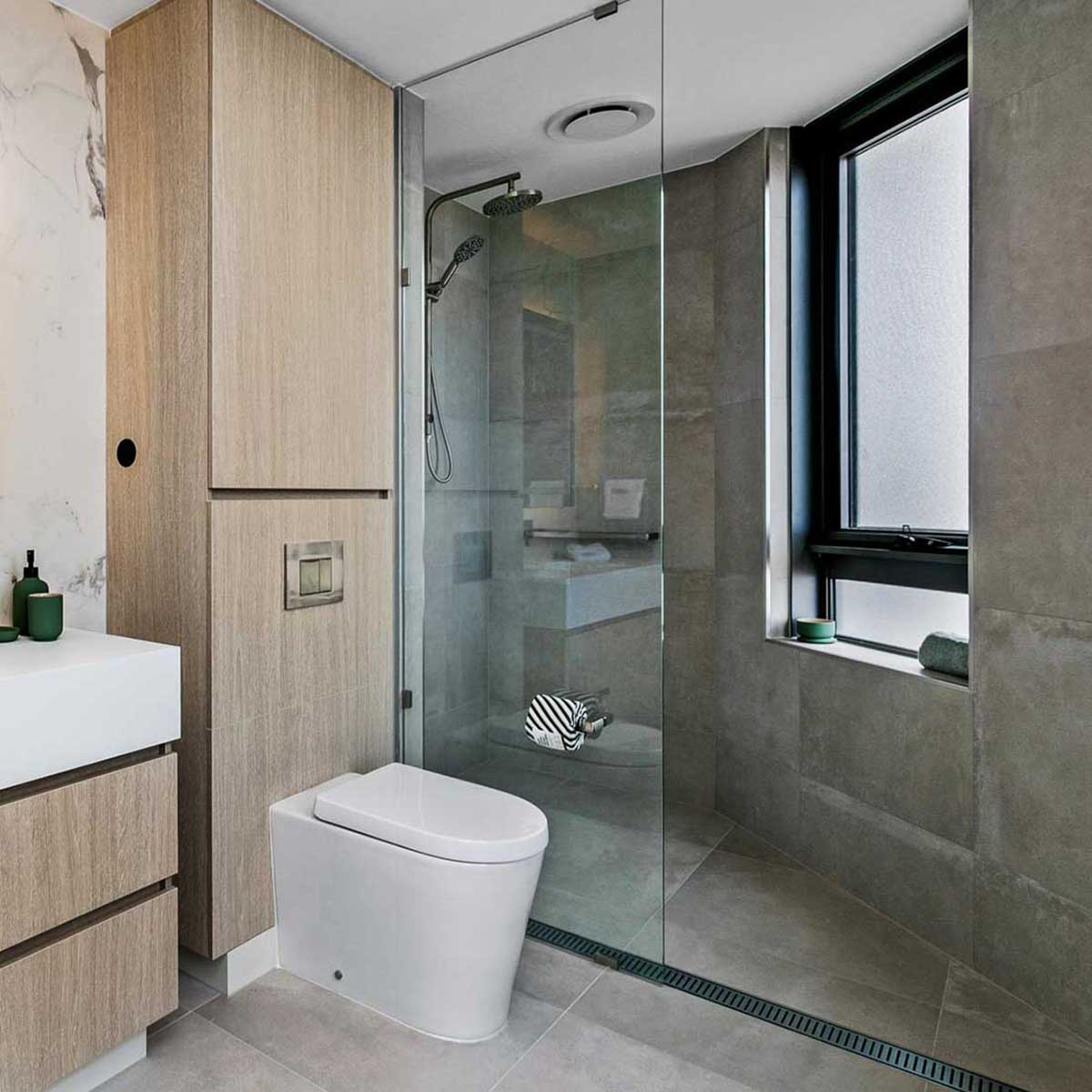 Modern bathroom with glass shower enclosure, toilet, wooden cabinets and Lauxes Grates Custom Linear Shower Drain NeXT Generation Midnight Black