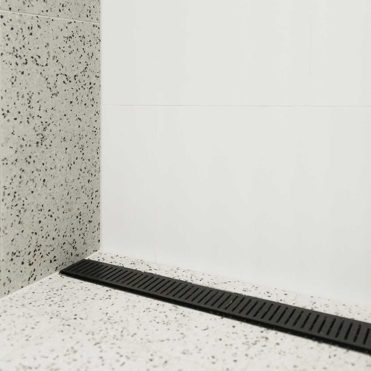 Lauxes Grates Custom Linear Shower Drain NeXT Generation Midnight Black on a speckled gray floor with white walls
