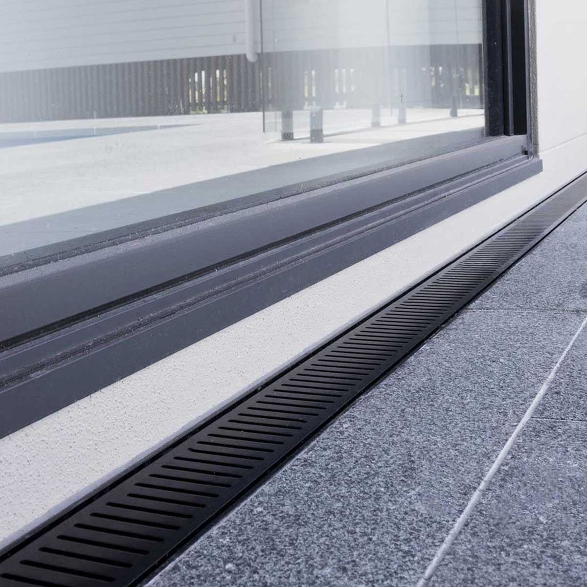 Close-up of a window with a black Lauxes Grates Custom Linear Shower Drain NeXT Generation Midnight Black on a building exterior.