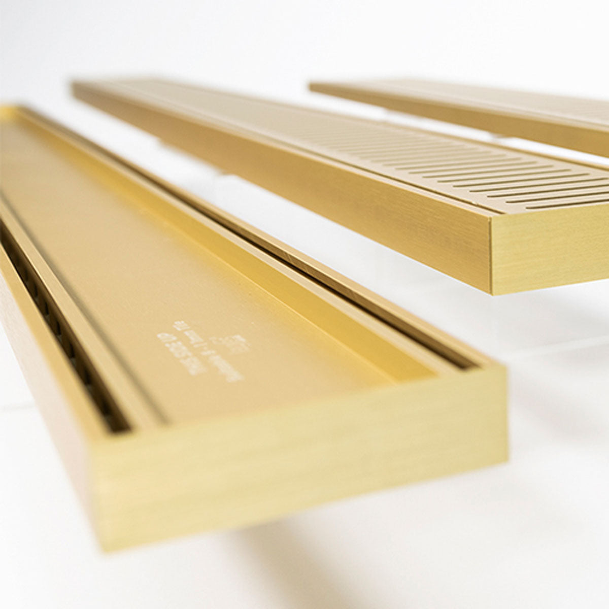 Close-up of a Lauxes Grates Custom shower drain Tile Insert in Matte Gold finish