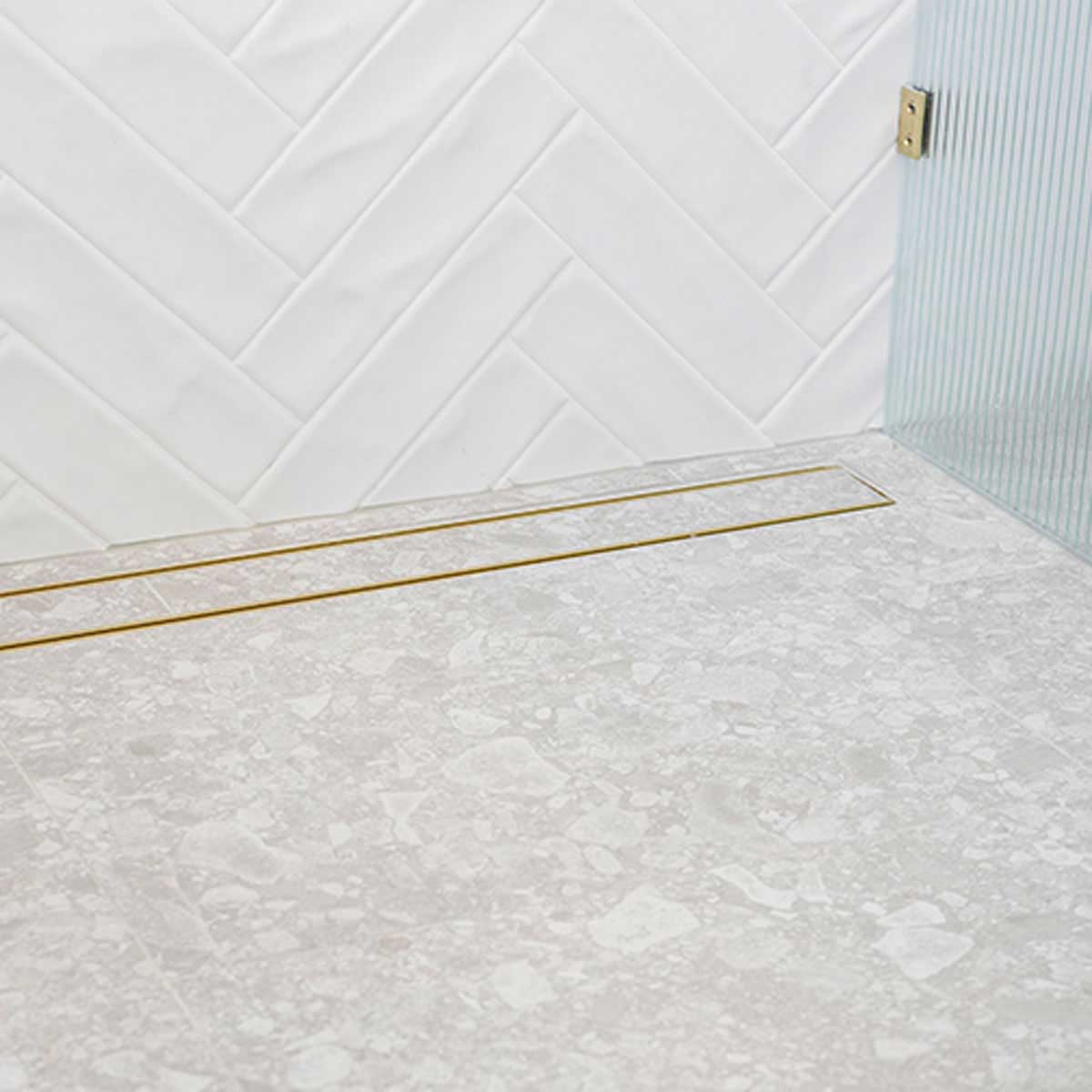 Close-up of a tiled floor with Lauxes Grates Custom shower drain Tile Insert in Matte Gold finish