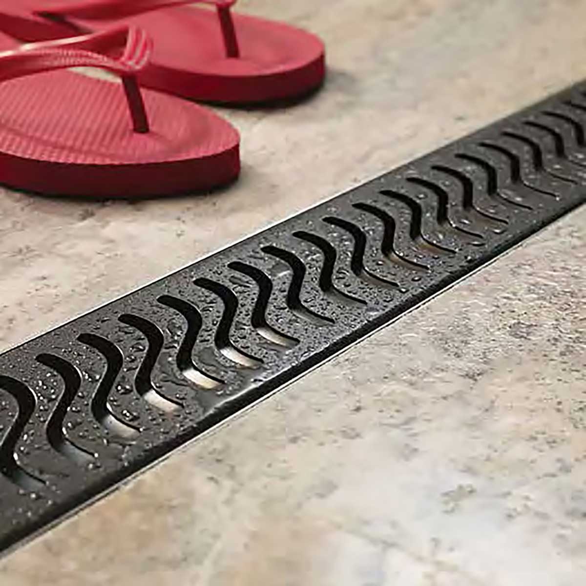 QuARTz Linear Shower Drain with Flag Grate - Oil Rubbed Bronze next to red flip flop in shower floor