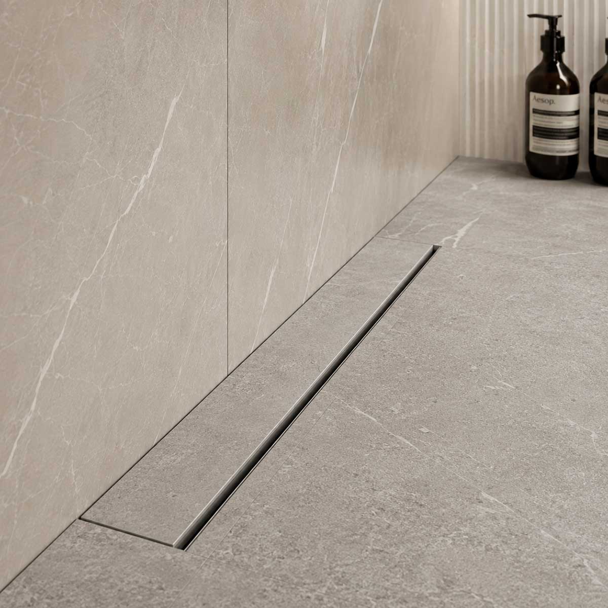 Invisible linear shower drain installed against tiled wall