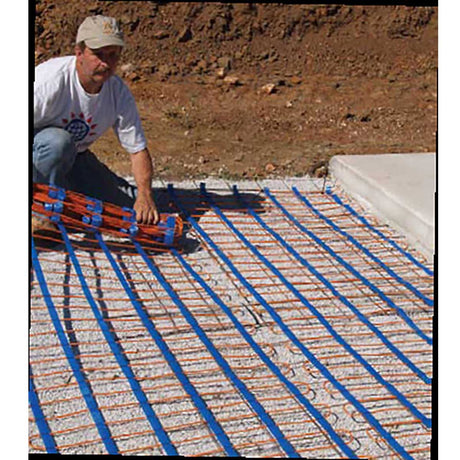 Person installing a heating system on a concrete floor with visible blue pipes.