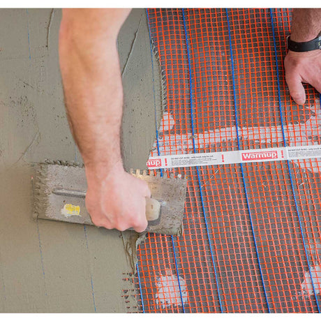 Warmup StickyMat applying a thinset to a floor with Warmup heating cable visible underneath