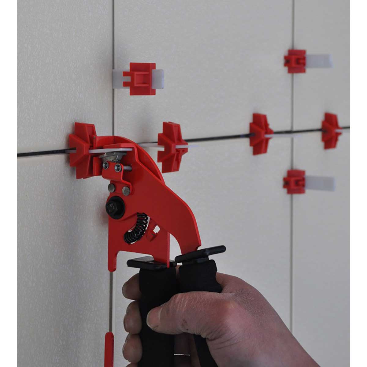 Hand using a red tile leveling system tool on a tiled wall.