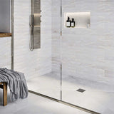 Modern shower with glass door, tiled walls, and a bench with a towel and Ebbe Square Shower Drain Grates