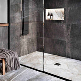 Modern bathroom with glass shower enclosure, black wall tiles, and gold fixtures with Ebbe Drains Unique Square Shower Drain Grate - Bubbles