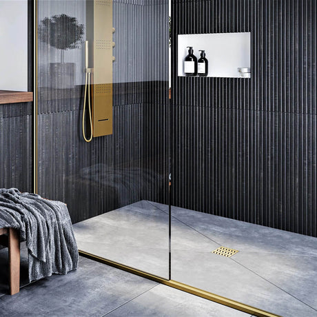 Modern bathroom with glass shower enclosure, black wall tiles, and gold fixtures with Ebbe Drains Unique Square Shower Drain Grate - Trend