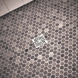 Hexagonal tile floor with a Ebbe Drains Unique Square Shower Drain Grate - Twister In brushed Nickel