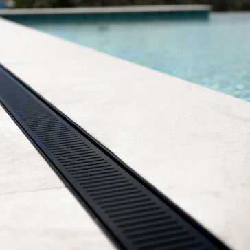Lauxes Grates Custom Linear Shower Drain NeXT Generation Midnight Black on a pool deck with water in the background