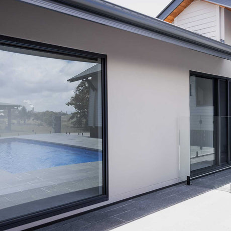Modern house exterior with large glass windows overlooking a pool with Lauxes Grates Custom Linear Shower Drain NeXT Generation Midnight Black Installed