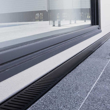 Close-up of a window with a black Lauxes Grates Custom Linear Shower Drain NeXT Generation Midnight Black on a building exterior.