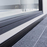 Close-up of a window with a black Lauxes Grates Custom Linear Shower Drain NeXT Generation Midnight Black on a building exterior.