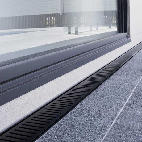 Close-up of a window with a black Lauxes Grates Custom Linear Shower Drain NeXT Generation Midnight Black on a building exterior.