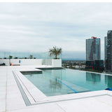 Modern rooftop pool with city skyline in the background and a Lauxes Grates Custom Linear shower Drain NeXT Generation - Silk Silver surrounding the pool around.
