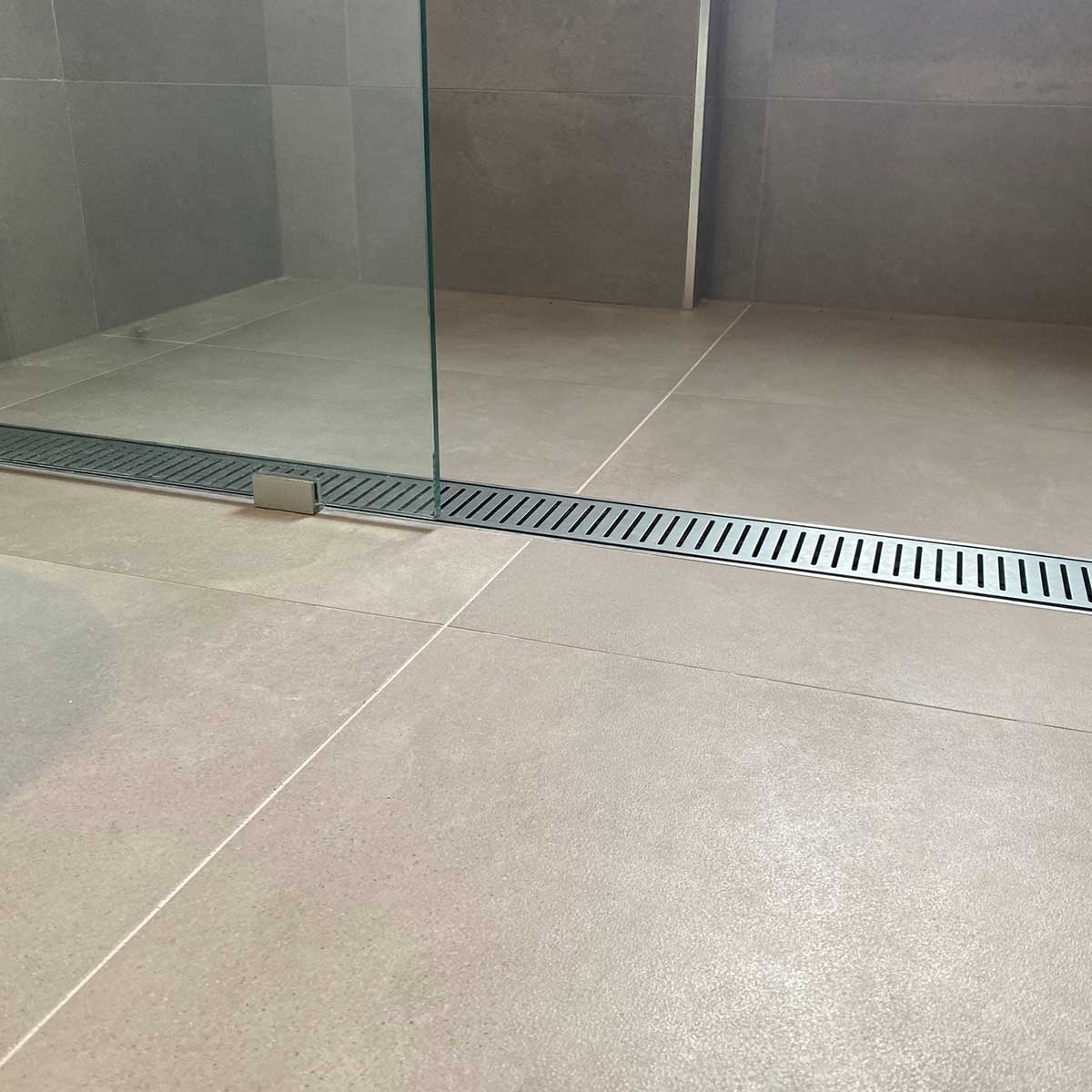 Tile shower floor with a Lauxes Grates Custom Linear shower Drain NeXT Generation - Silk Silver and glass wall
