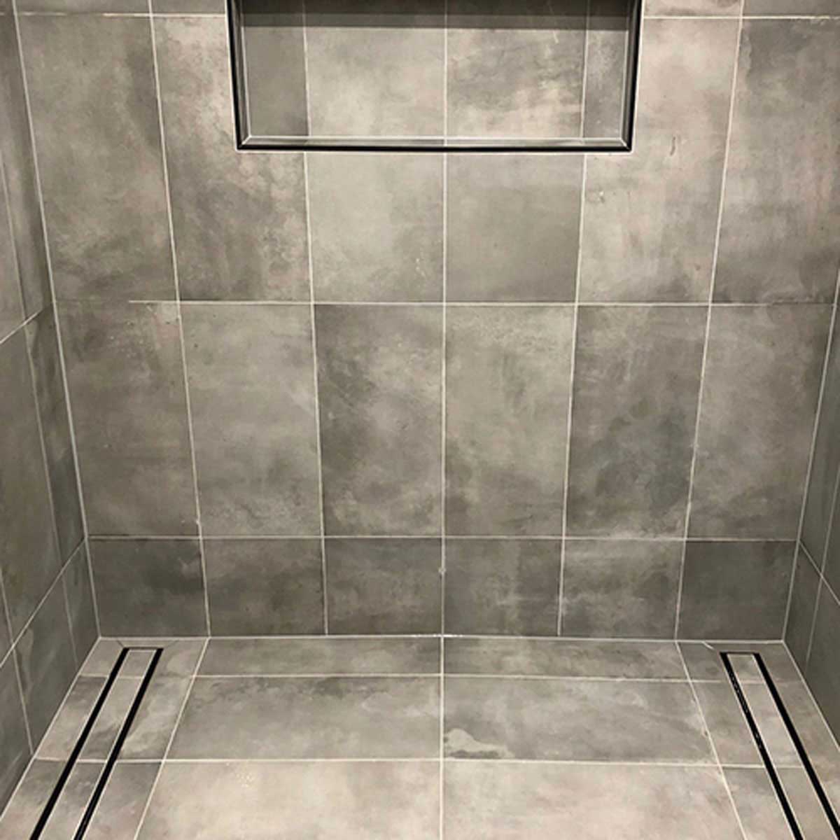 Close-up of a tiled floor with Lauxes Grates Custom shower drain Tile Insert in Midnight Black
