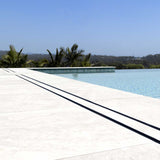 Close-up of a tiled floor with Lauxes Grates Custom shower drain Tile Insert in Midnight Black around the pool
