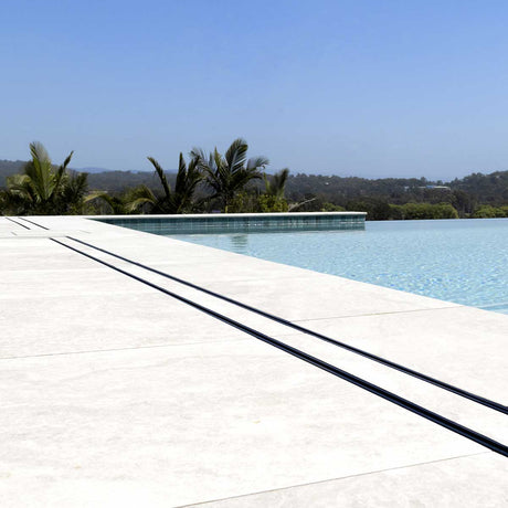 Close-up of a tiled floor with Lauxes Grates Custom shower drain Tile Insert in Midnight Black around the pool