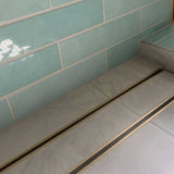Close-up of a tiled floor with Lauxes Grates Custom shower drain Tile Insert in Matte Gold finish 