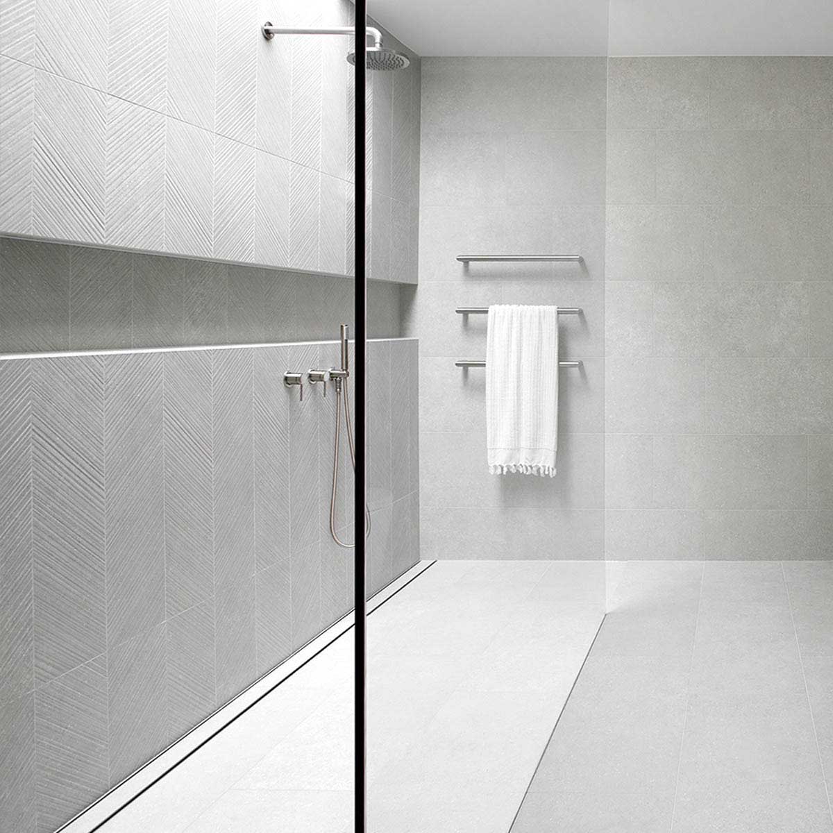 Modern bathroom with glass shower enclosure and towel rack with Close-up of a tiled floor with Lauxes Grates Custom shower drain Tile Insert in Silk Silver finish 