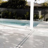 Glass pool fence with a view of a swimming pool and Close-up of a tiled floor with Lauxes Grates Custom shower drain Tile Insert in Silk Silver finish 