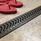 QuARTz Linear Shower Drain with Flag Grate - Oil Rubbed Bronze next to red flip flop in shower floor
