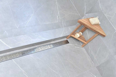 Gray bath mat and bottle near a Serenedrain broken lane shower drain on a tiled floor