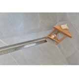 SereneDrain broken lane in polished chrome finish with a Teak caddy and bath sponge on a gray tiled floor.
