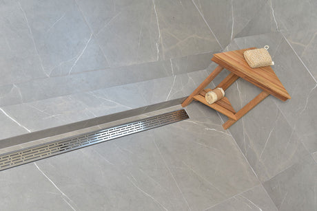 SereneDrain broken lane in polished chrome finish with a Teak caddy and bath sponge on a gray tiled floor.