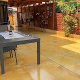 Outdoor patio with a dining table and chairs on a stone floor, surrounded by greenery.