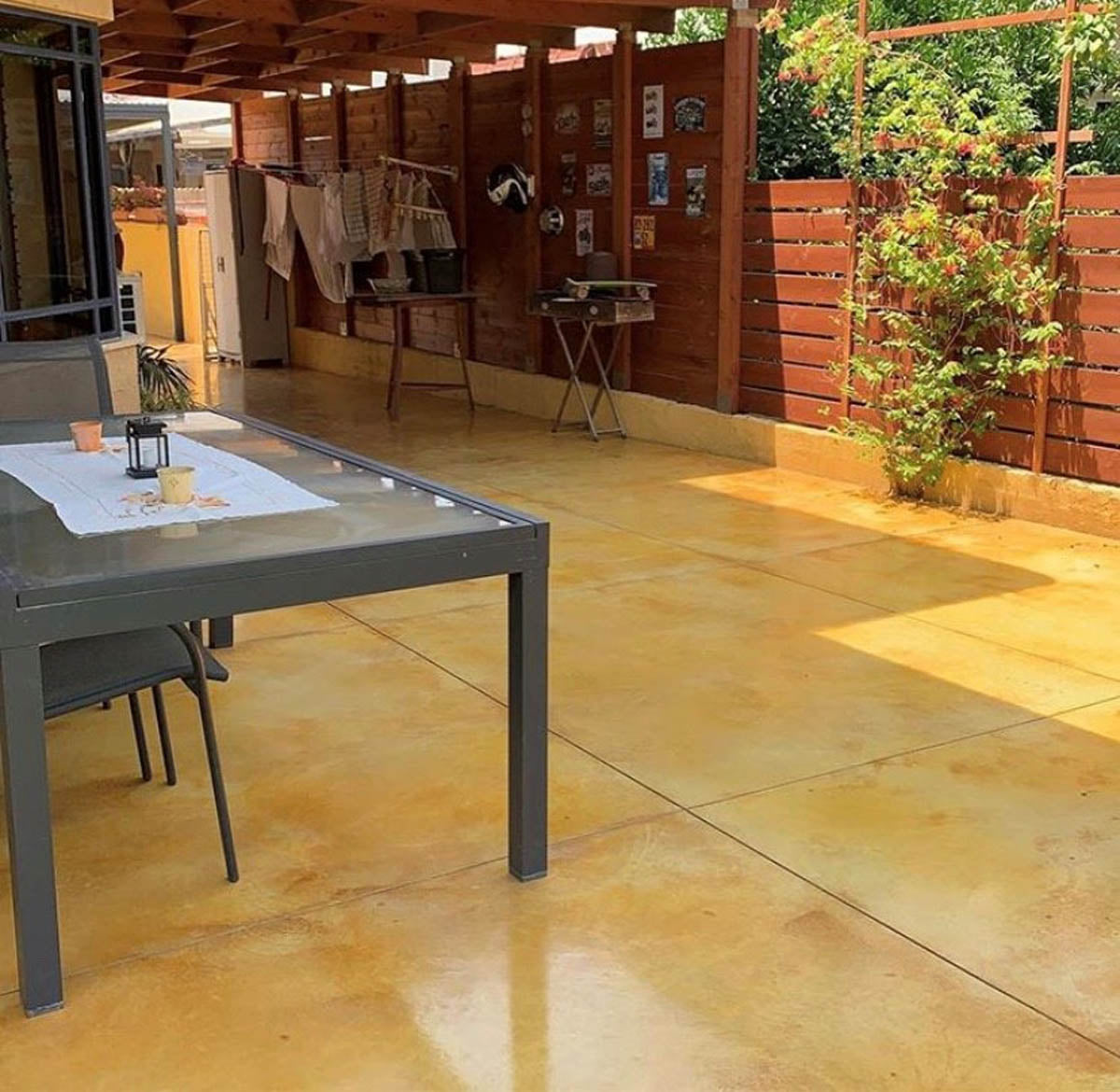 Outdoor patio with a dining table and chairs on a stone floor, surrounded by greenery.