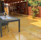 Outdoor patio with a dining table and chairs on a stone floor, surrounded by greenery.