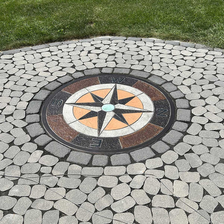 Smith Paint Colorful stains Decorative concrete mosaic compass design inlaid into a cobblestone patio surrounded by green grass.