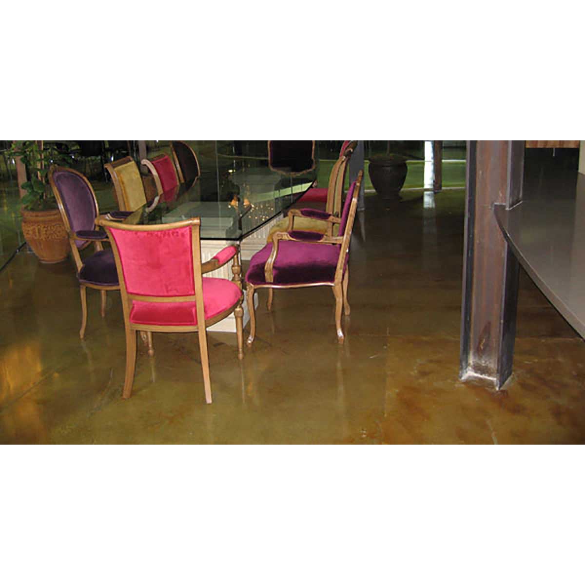 Dining area with chairs and a glass table on a polished concrete floor.