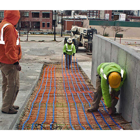 Workers installing heating cables on a concrete surface with a cityscape in the background.
