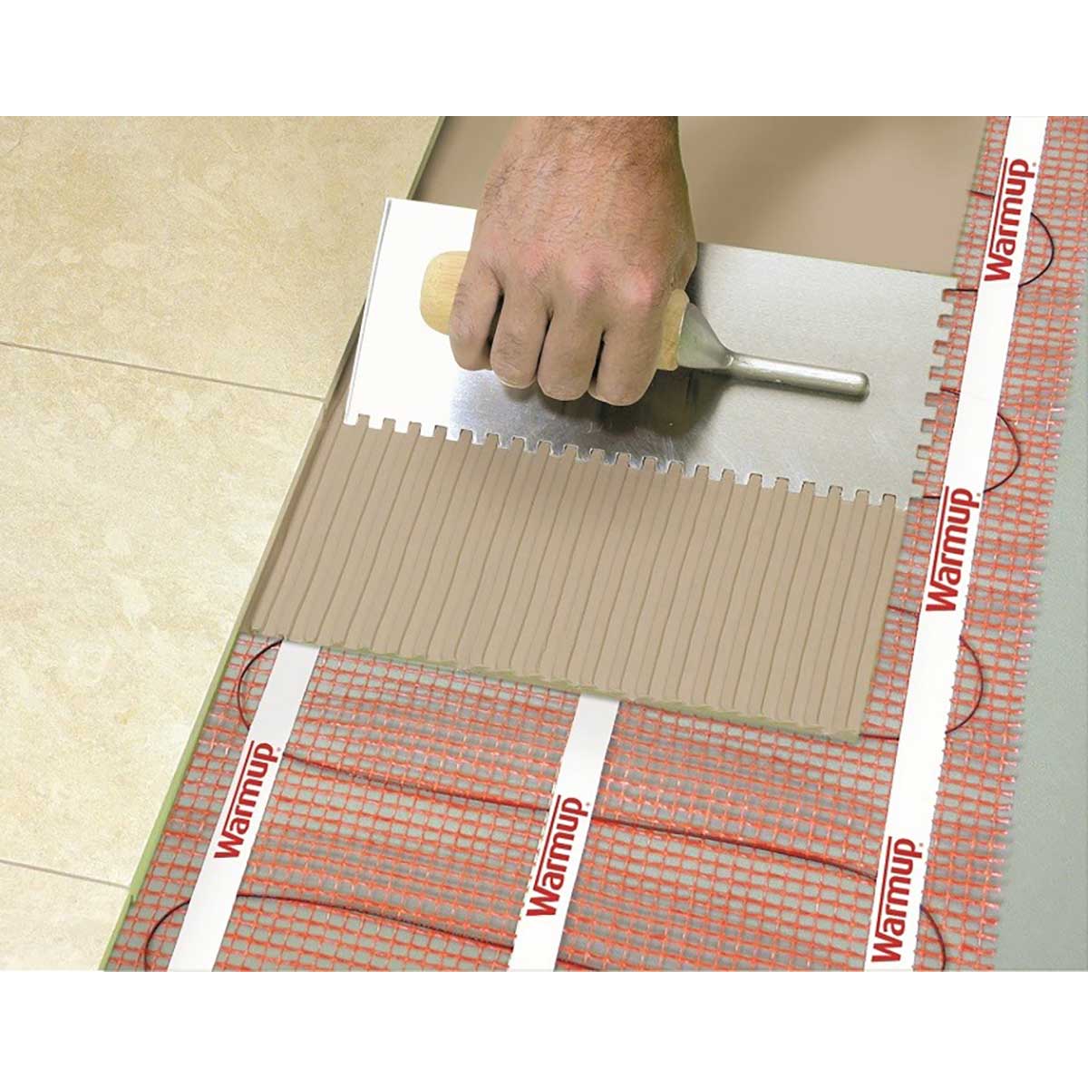 Warmup StickyMat applying a tile to a floor with Warmup heating cable visible underneath